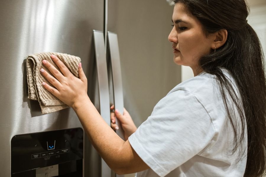 Pessoa limpando geladeira por dentro com pano e produtos caseiros