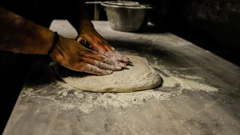 Pessoa sovando massa de pizza caseira sobre bancada enfarinhada
