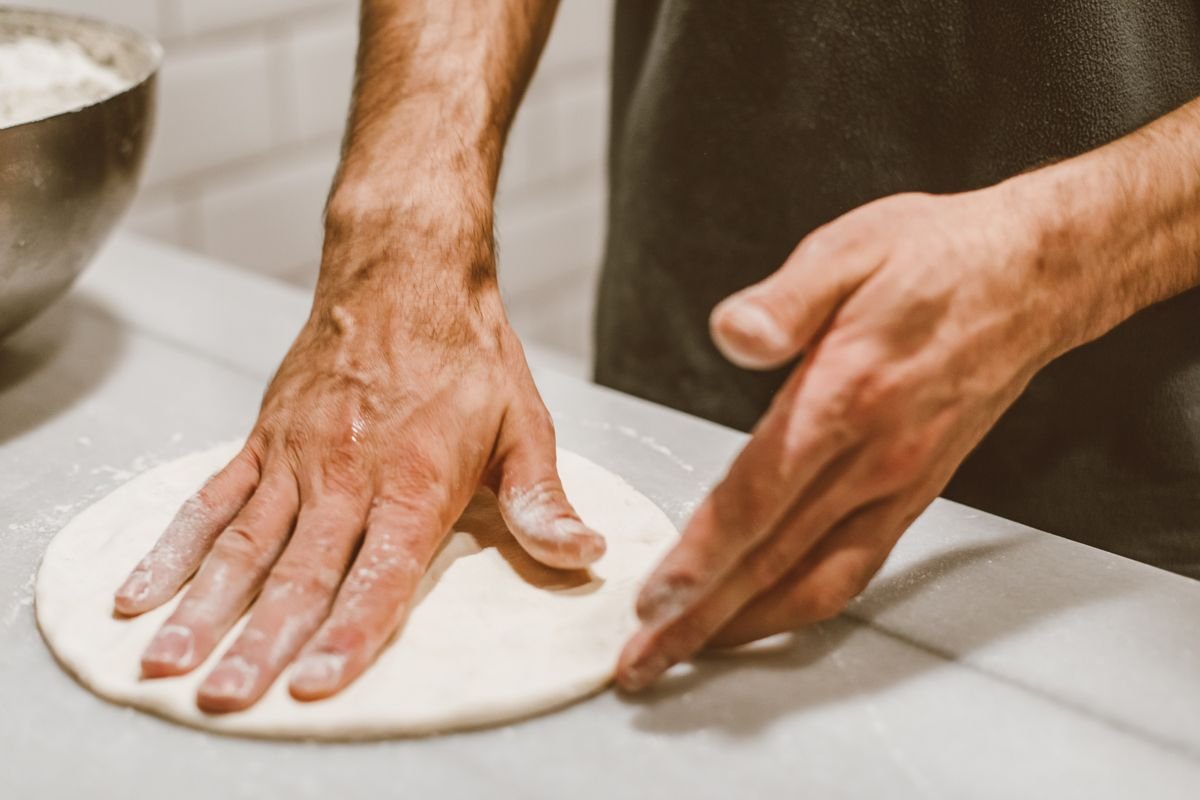 Maos moldando massa de pizza caseira com farinha