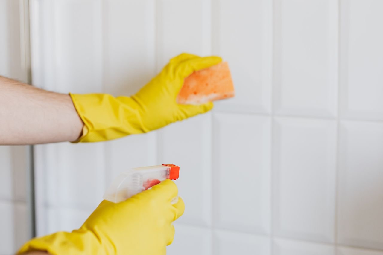 Pessoa usando luvas amarelas limpando rejunte de azulejo branco com esponja