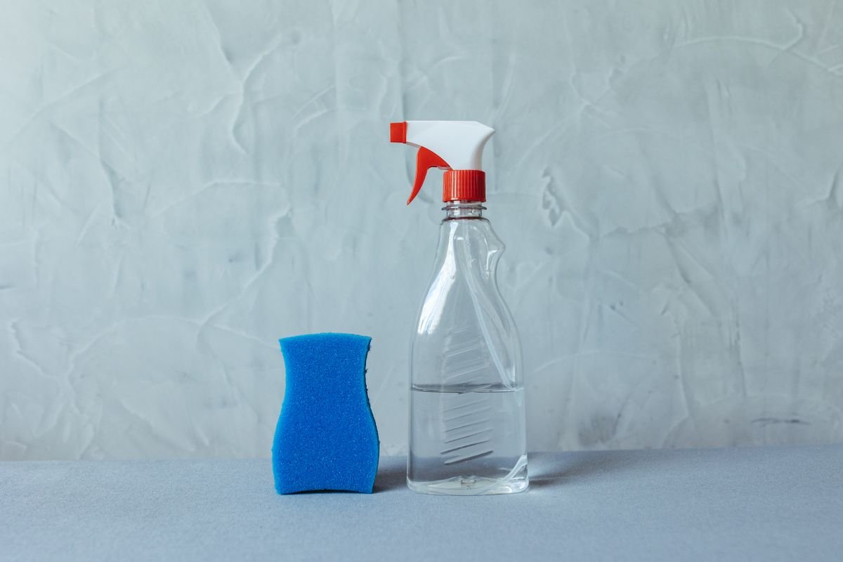 Materiais para limpar tênis branco: spray, esponja e sabão em superfície cinza