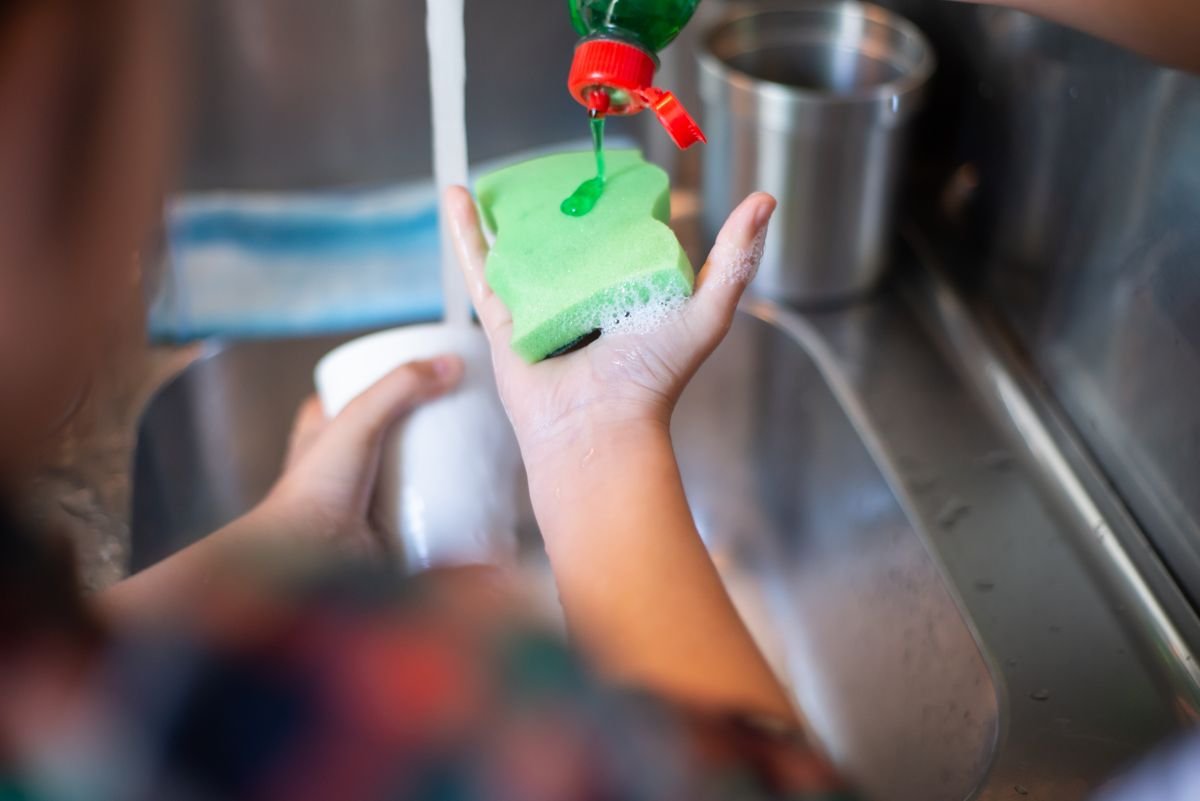 Mãos despejando detergente na esponja para limpar tênis branco