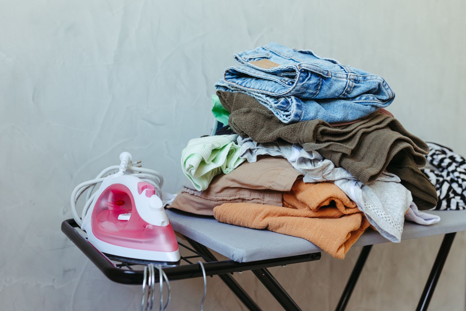 Pilha de roupas recém-passadas ao lado de ferro a vapor sobre tábua de passar