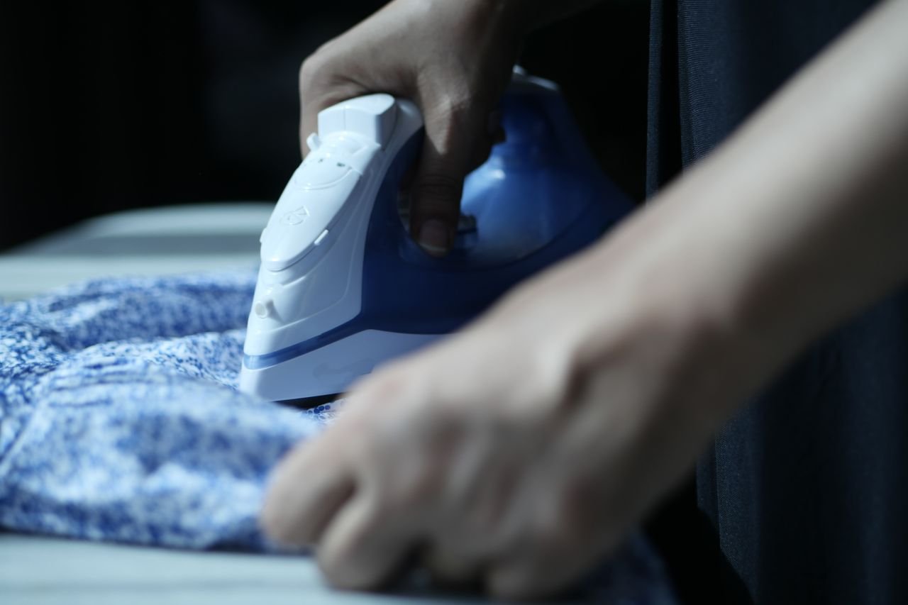 Mãos utilizando ferro elétrico de passar sobre tecido azul