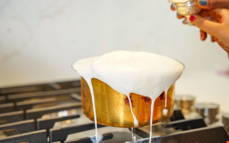 Leite sendo aquecido em panela dourada para preparo de leite condensado caseiro