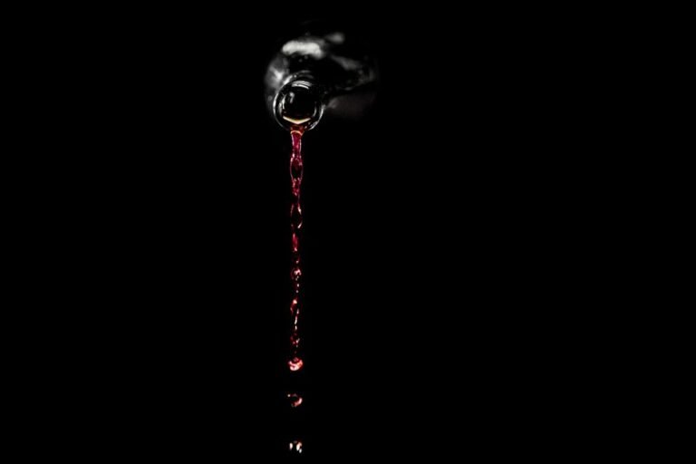 Vinho tinto sendo derramado de uma garrafa escura sobre fundo preto
