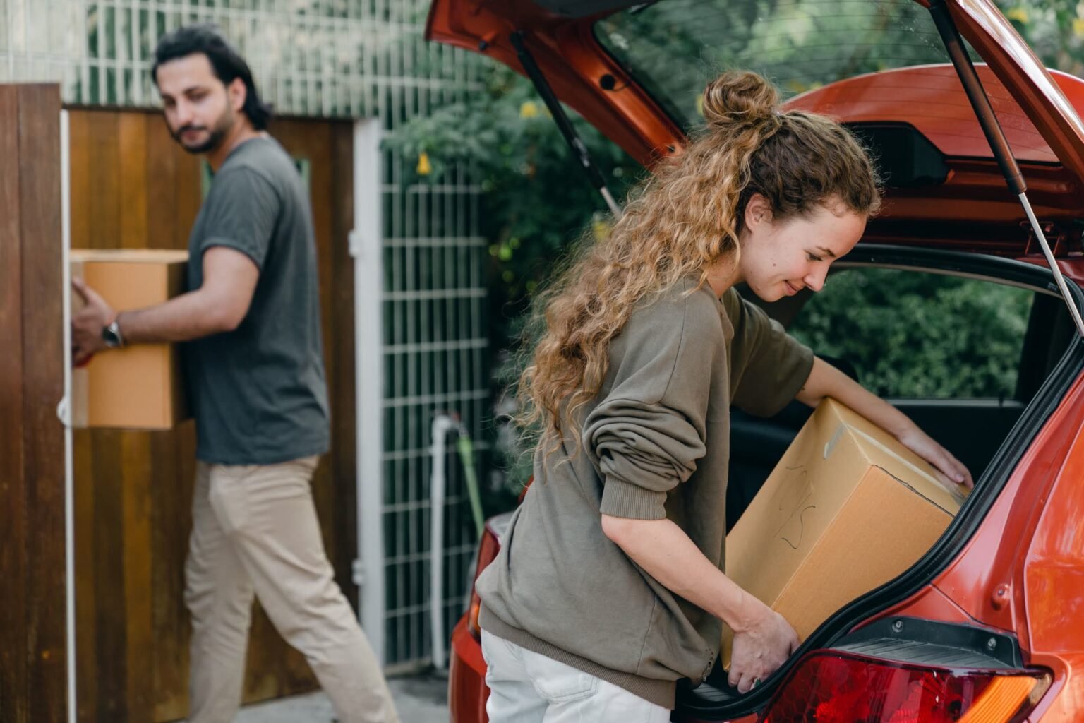 Casal retirando caixas do porta-malas do carro na mudança: como organizar o porta-malas para transporte e viagem