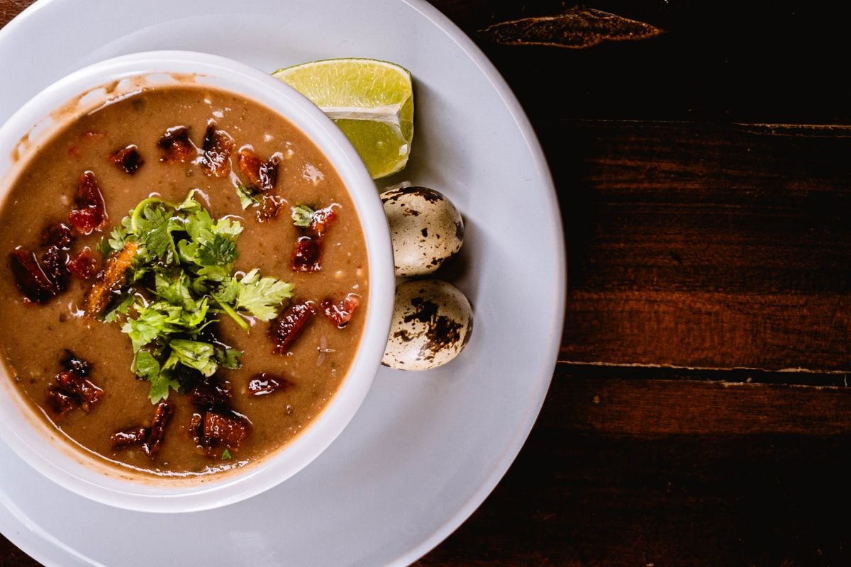 Caldo de feijão cremoso com cheiro verde, limão e ovos servido em mesa de madeira