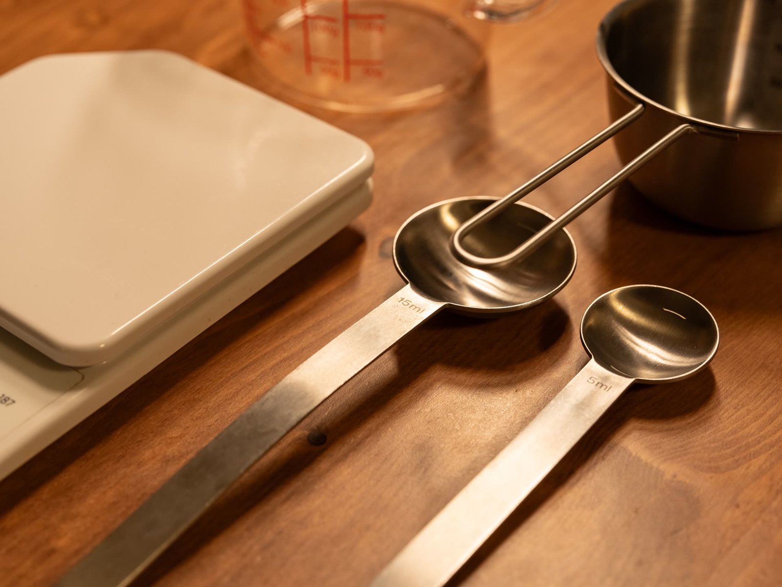 Utensílios de medição em bancada de madeira, com balança digital, xícaras e colheres: tabela de medidas na cozinha