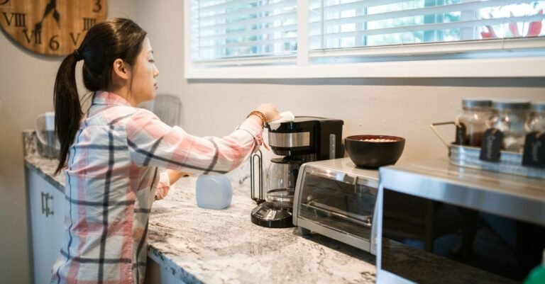 Pessoa limpando cafeteira eletrica com pano na pia da cozinha