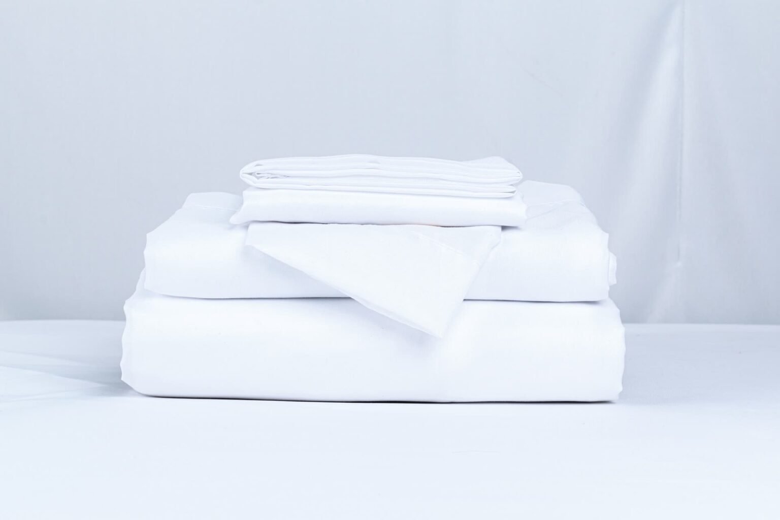 Pilha de lençóis e fronhas brancos dobrados: peças que compõem um jogo de cama de casal e como conferir o kit antes de comprar