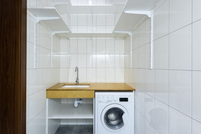 Lavanderia moderna com azulejos brancos, maquina de lavar e prateleiras