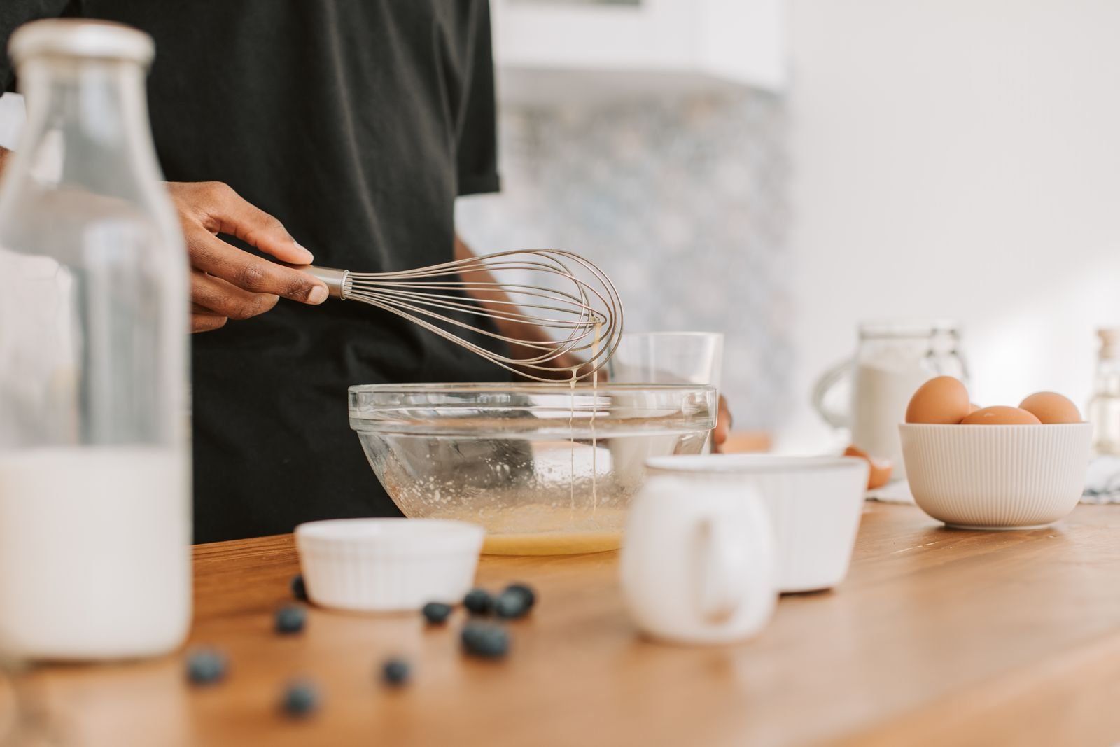 Pessoa batendo ingredientes com fouet em uma tigela de vidro sobre a bancada