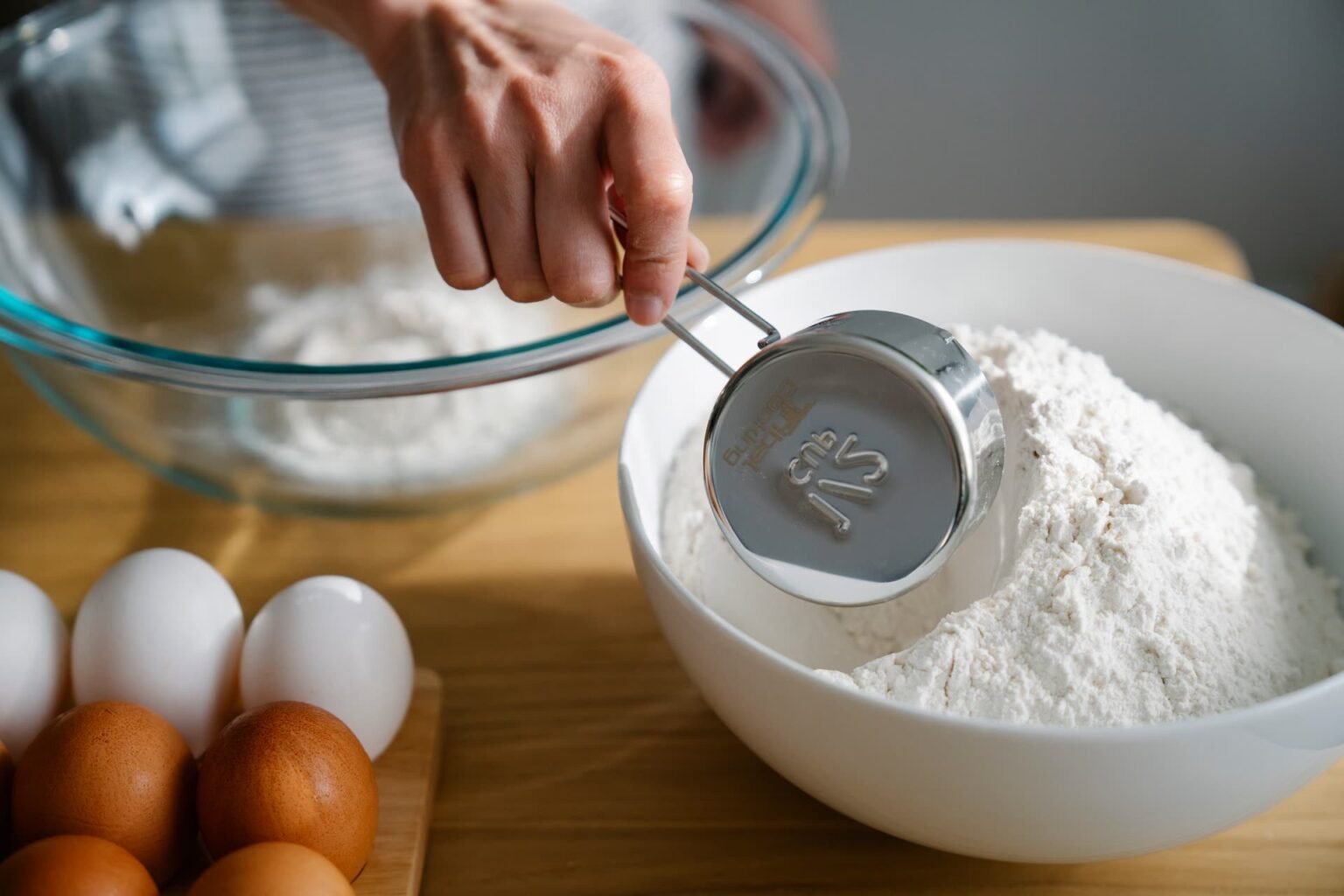 Mão tirando farinha de um bowl com colher medidora na cozinha: como aplicar a tabela de medidas na cozinha sem compactar o ingrediente
