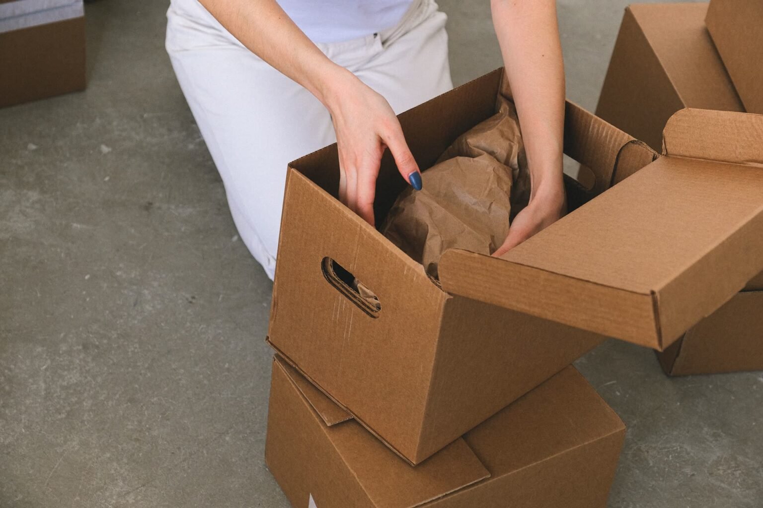 Mulher embalando objetos com papel em caixa de papelão, parte de como organizar uma mudança de casa