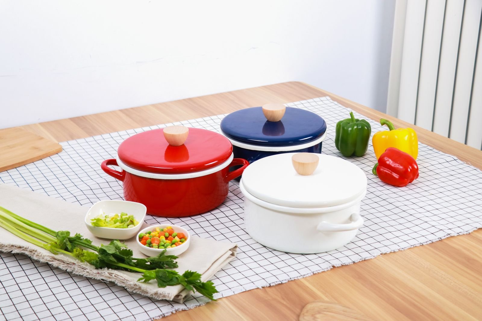 Panelas esmaltadas coloridas com pimentoes e temperos sobre mesa de madeira