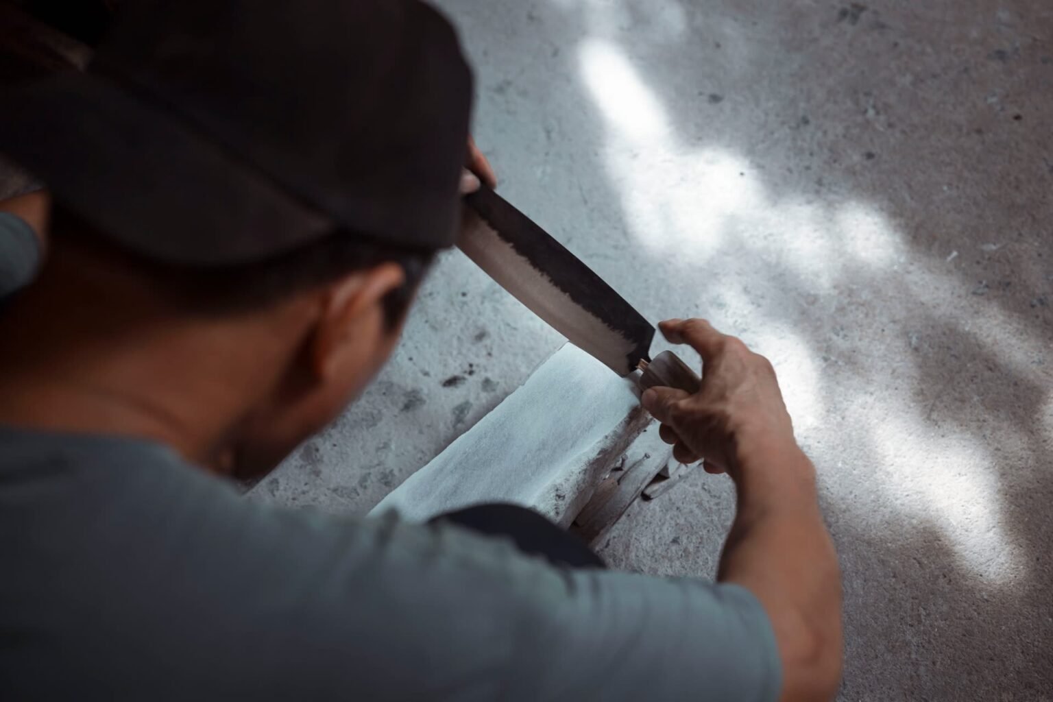 Homem afiando faca em pedra de amolar tradicional: como afiar faca em casa com ângulo constante e pedra molhada
