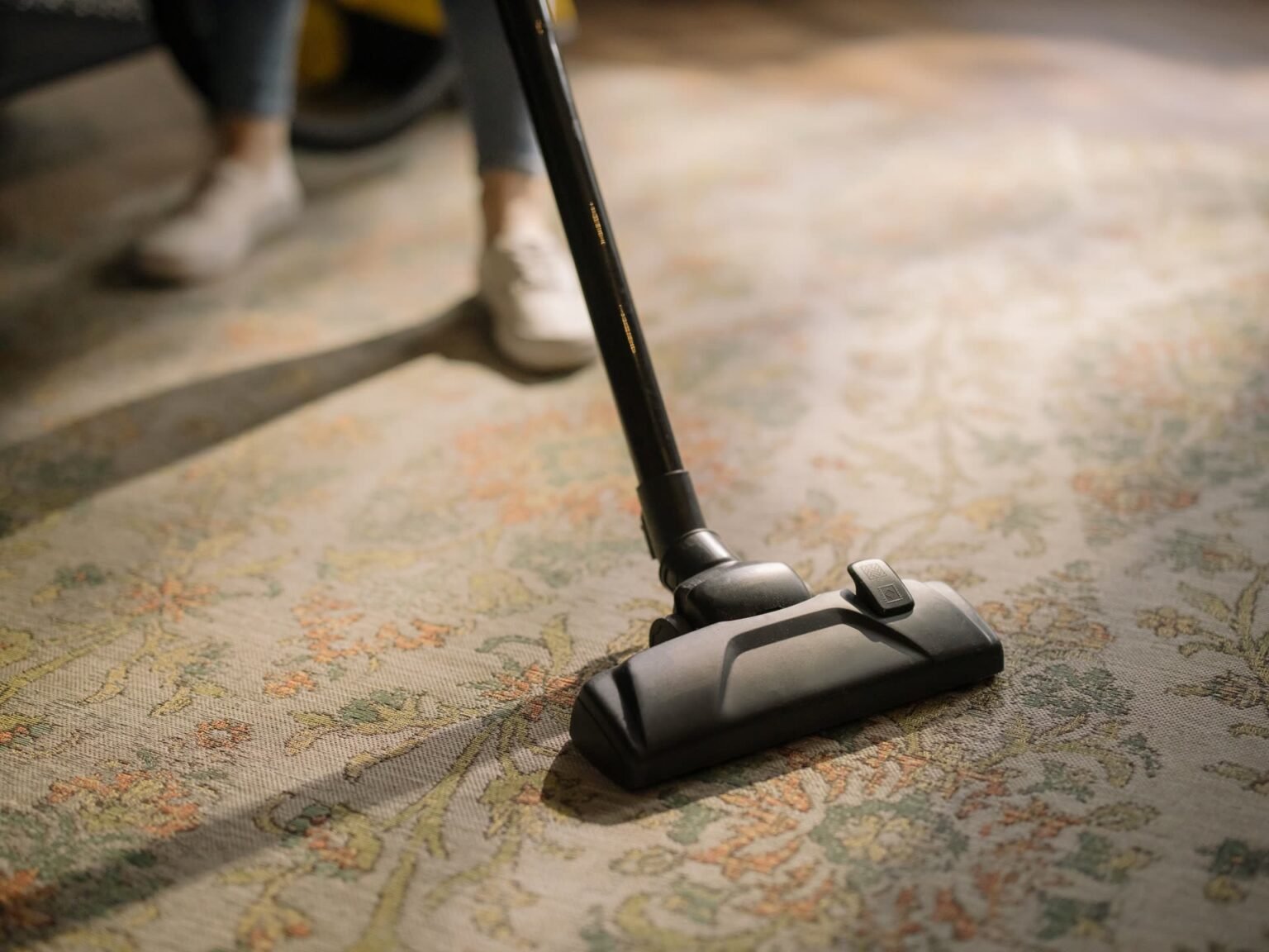Aspirador de pó sobre tapete estampado em sala iluminada, primeiro passo de como limpar tapete em casa